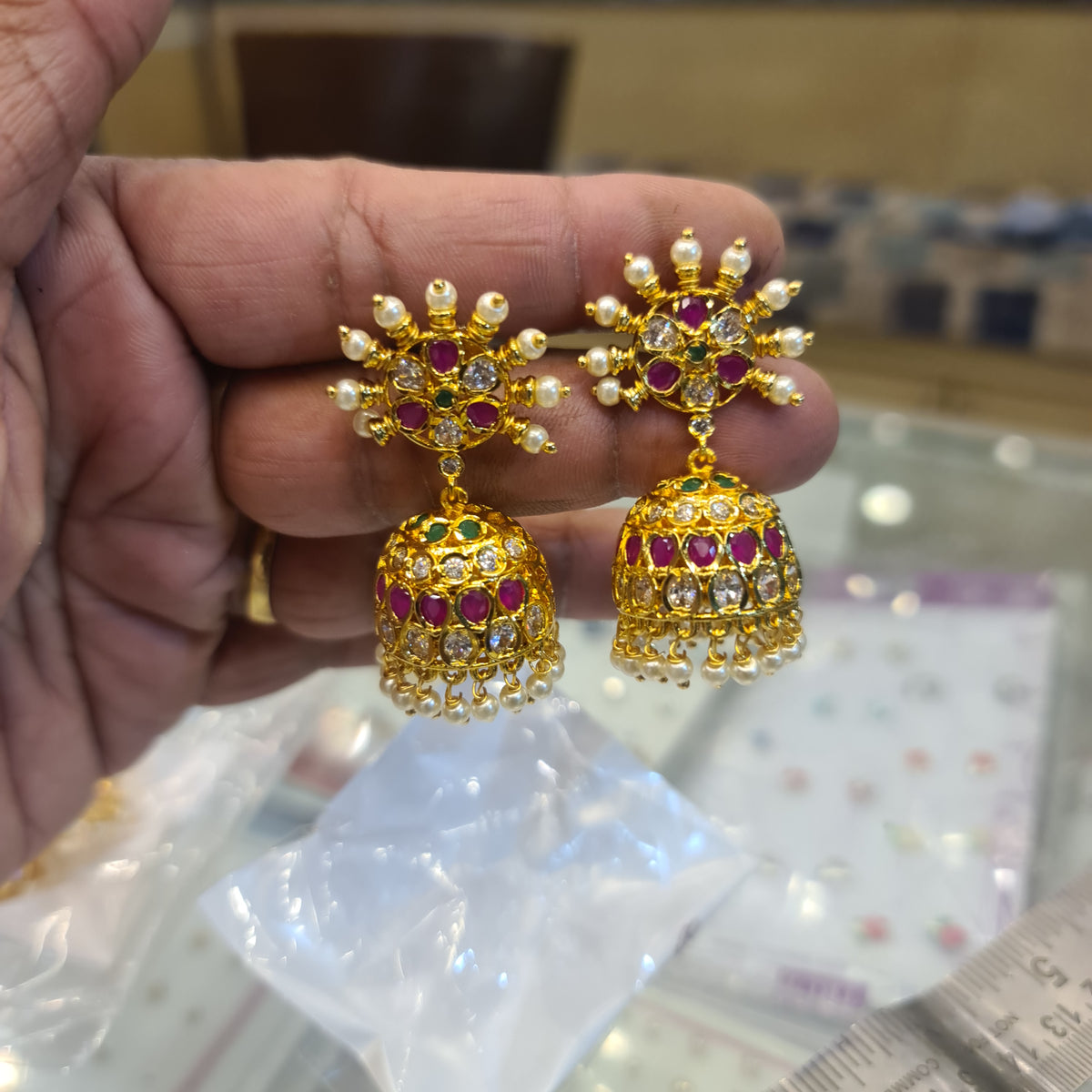 Gold earrings with gemstones held in a hand against a blurred background