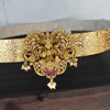 Gold belt with intricate design and gemstones held by a hand on a dark surface.