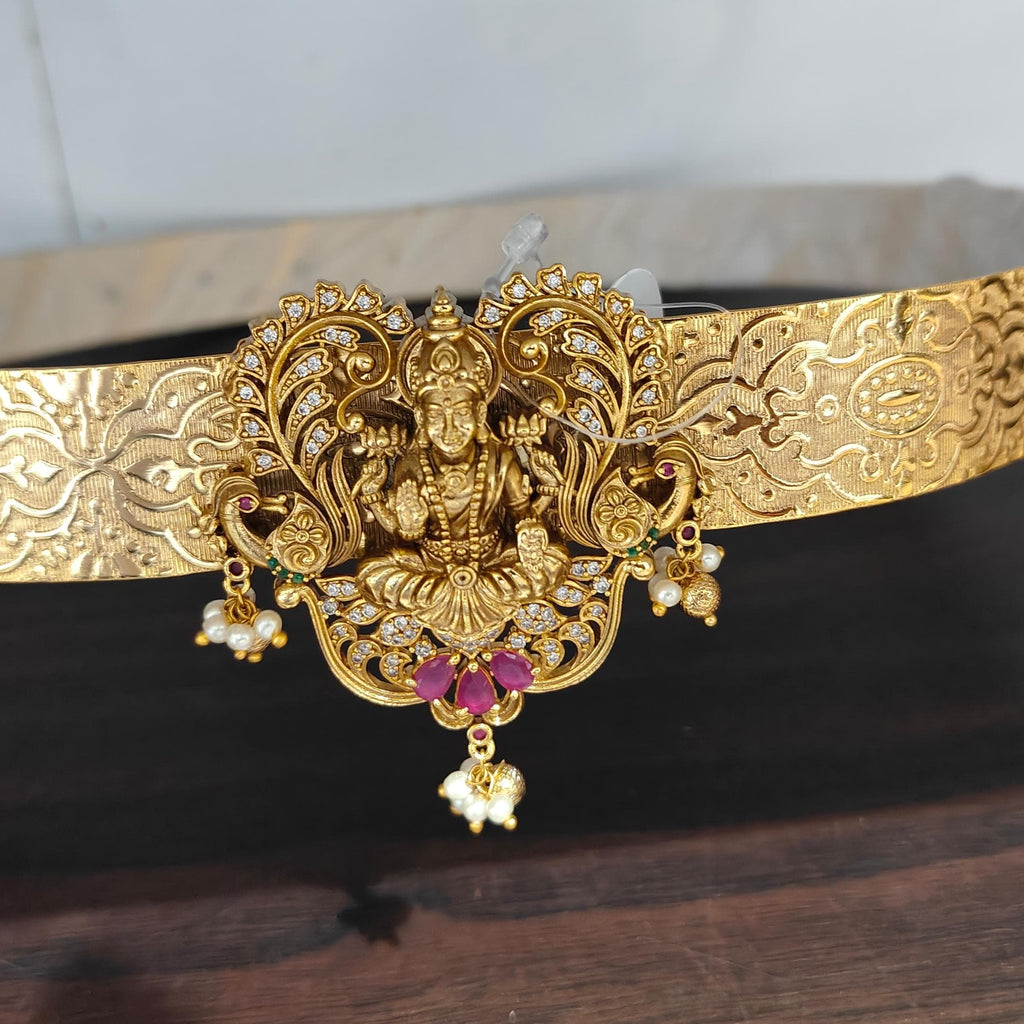 Gold belt with intricate design and gemstones held by a hand on a dark surface.