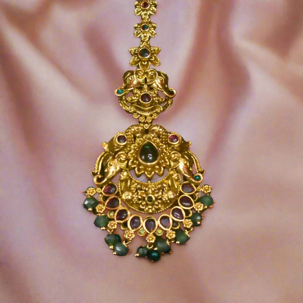 Decorative gold pendant with green stones on a pink fabric background
