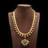 Gold necklace with green and red accents on a brown mannequin against a black background