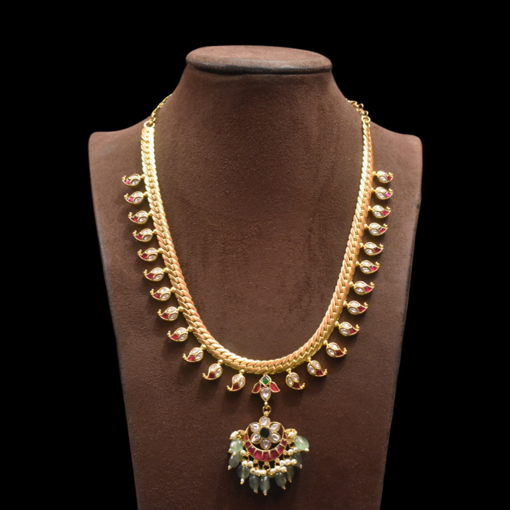 Gold necklace with green and red accents on a brown mannequin against a black background