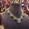 Decorative gold necklace with a blue gemstone on a brown mannequin against a blurred jewelry store background.
