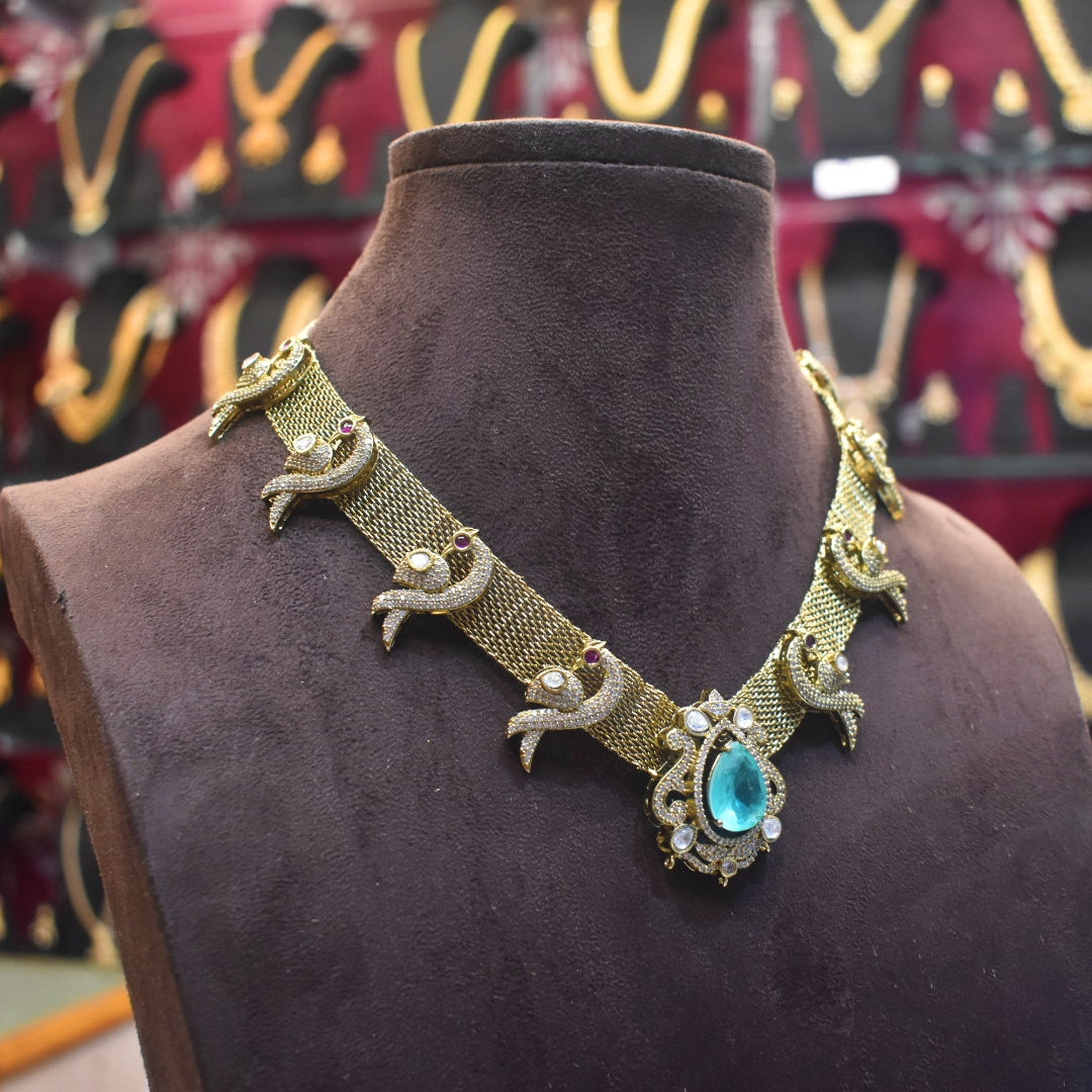 Decorative gold necklace with a blue gemstone on a brown mannequin against a blurred jewelry store background.