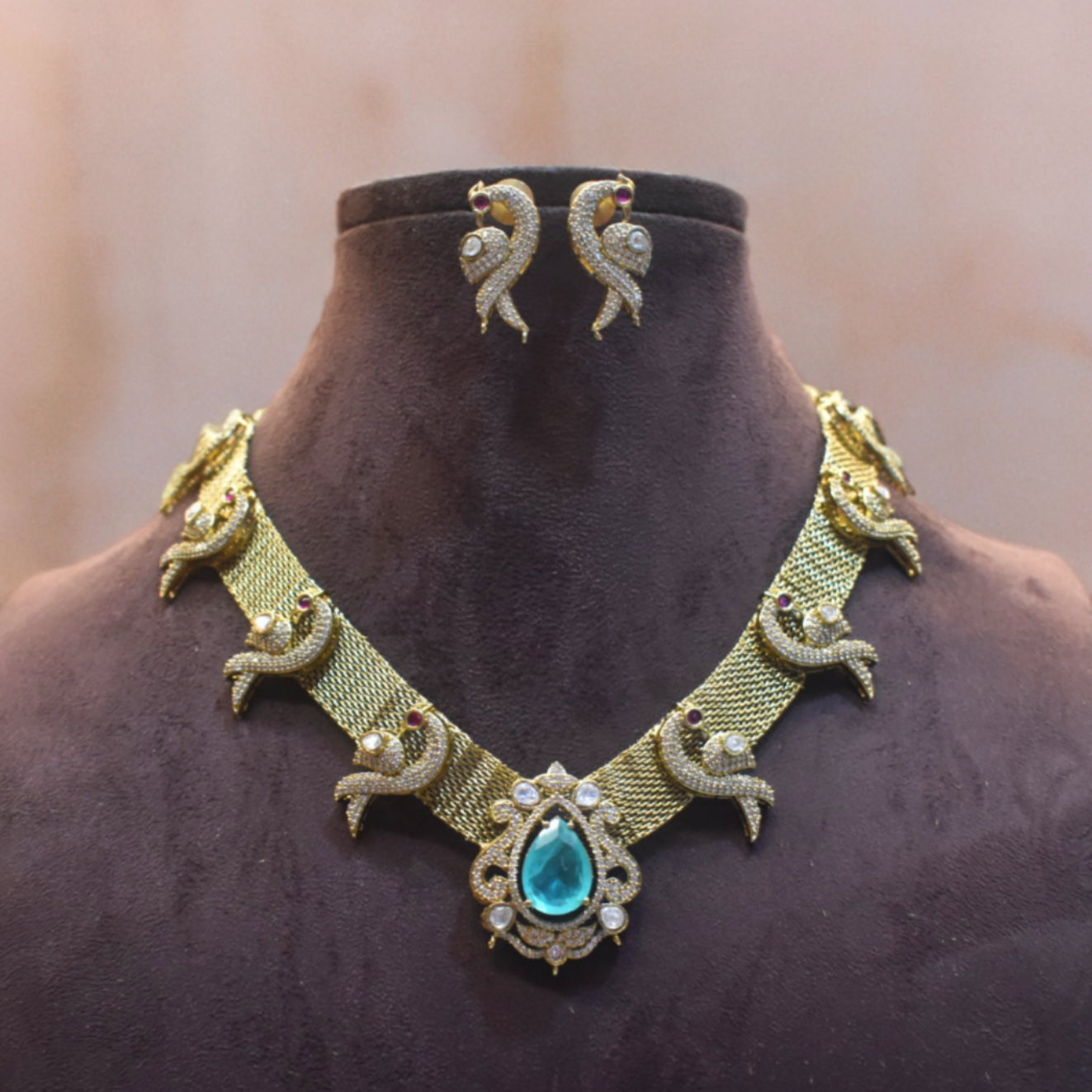 Gold necklace with a blue gemstone and matching earrings on a mannequin.