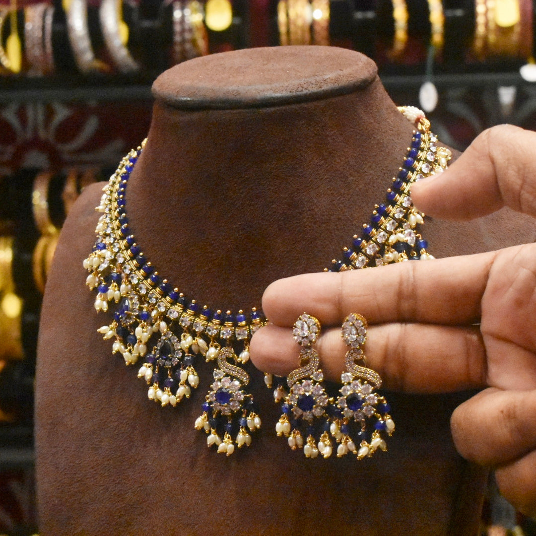 Gold and blue jewelry set on a mannequin bust with a hand holding an earring.