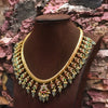 Gold necklace with green stones on a brown mannequin against a textured background
