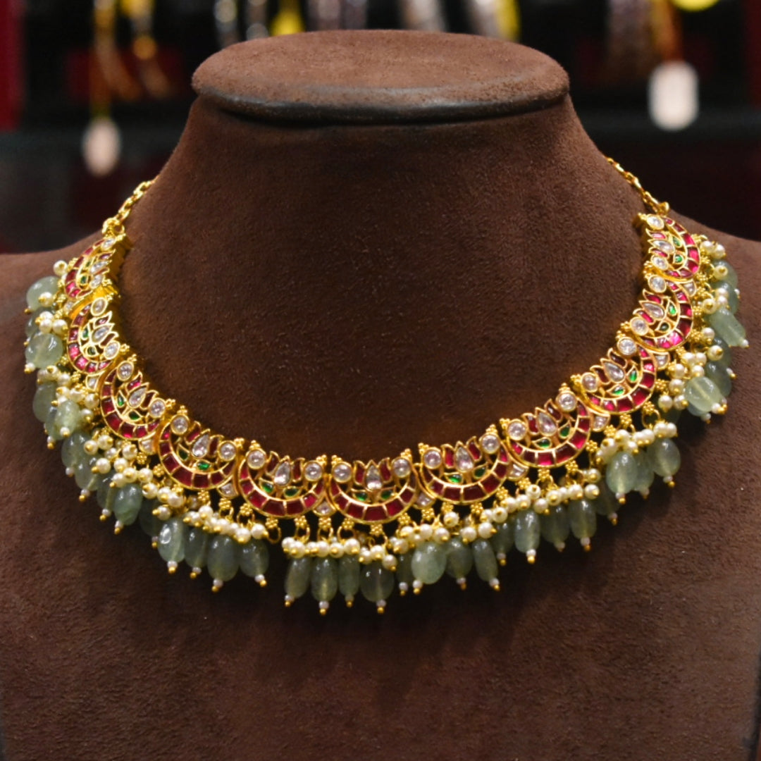 Ornate necklace with green beads and gold accents on a brown velvet stand.