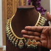 Gold necklace and earrings on a brown mannequin with a hand holding the earrings.