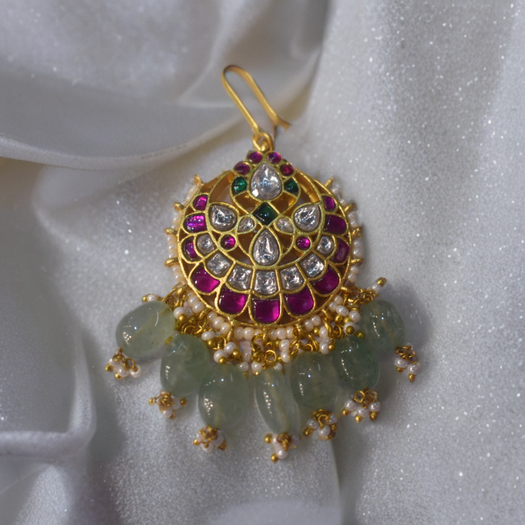 Decorative pendant with gemstones and gold accents on a white fabric background