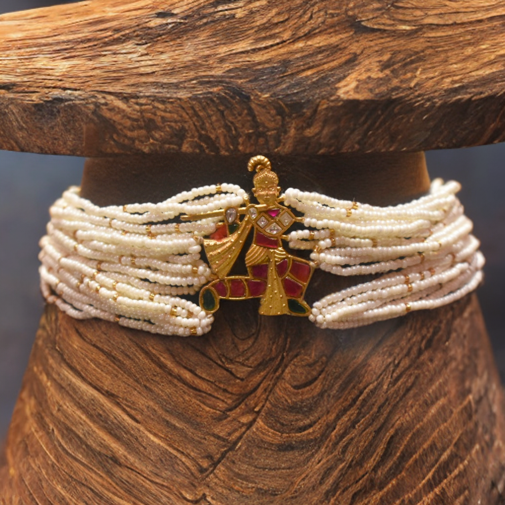 Pearl choker with a decorative gold and red pendant on a wooden stand.