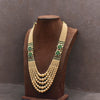 Gold necklace with green accents on a brown mannequin against a dark background
