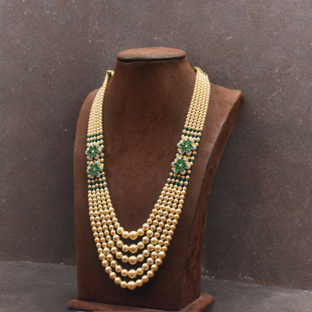Gold necklace with green accents on a brown mannequin against a dark background