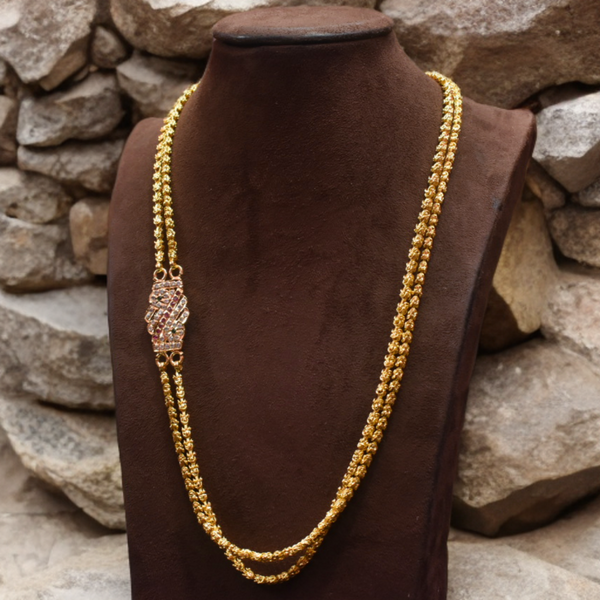Gold necklace on a brown mannequin against a stone wall background