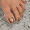 Toe with gold glitter nail polish and a gold ring on a marble surface