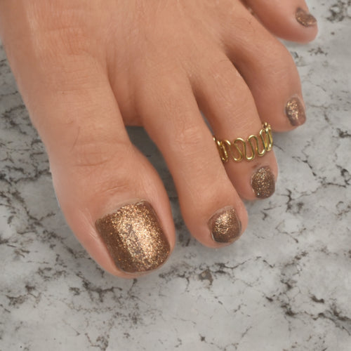Toe with gold glitter nail polish and a gold ring on a marble surface