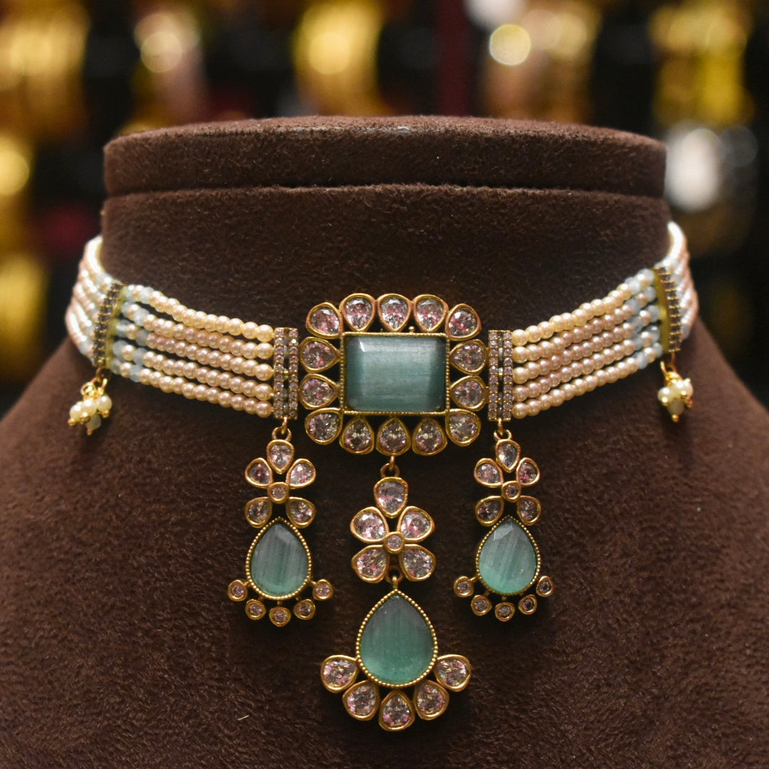 Decorative necklace with green gemstones and pearl-like strands on a brown stand.