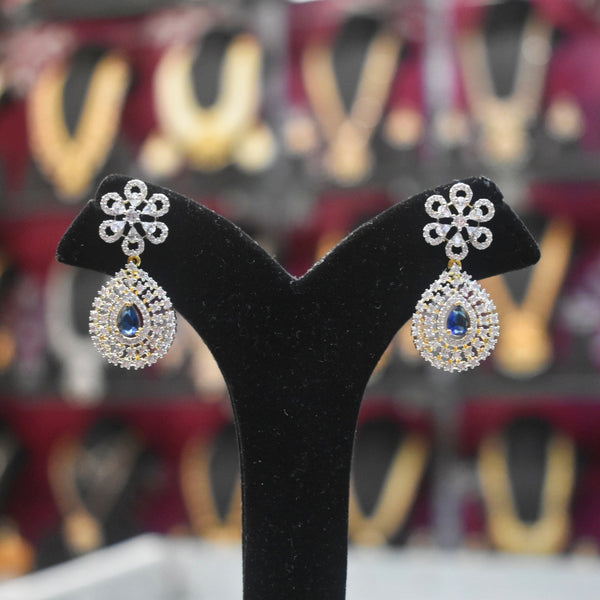 Pair of silver earrings with blue gemstones on a black stand against a blurred background.