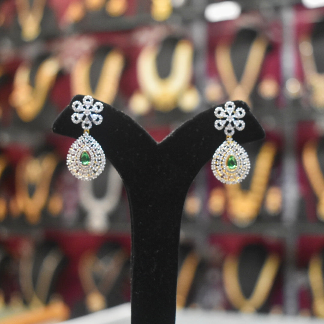 Pair of diamond earrings with green gemstones on a black stand against a blurred background.