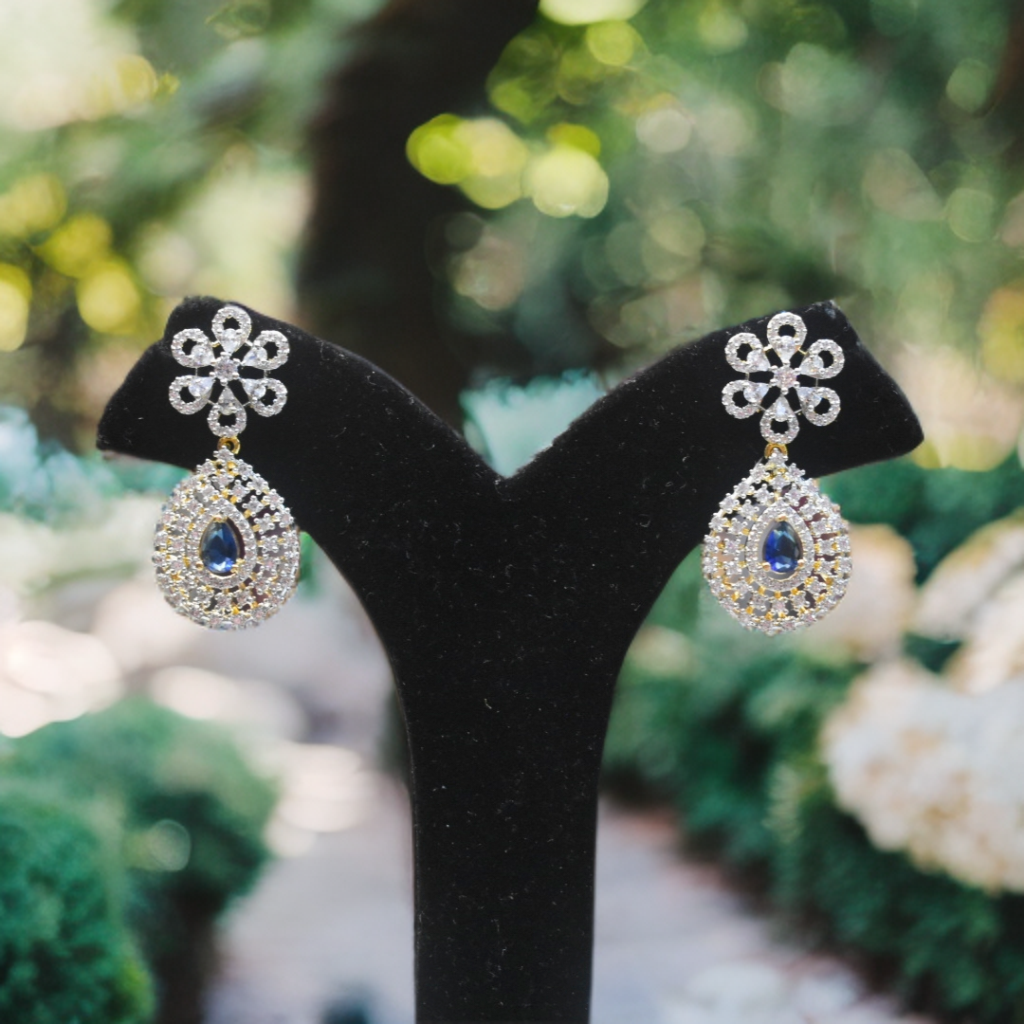 Pair of silver earrings with blue gemstones on a black stand against a blurred natural background