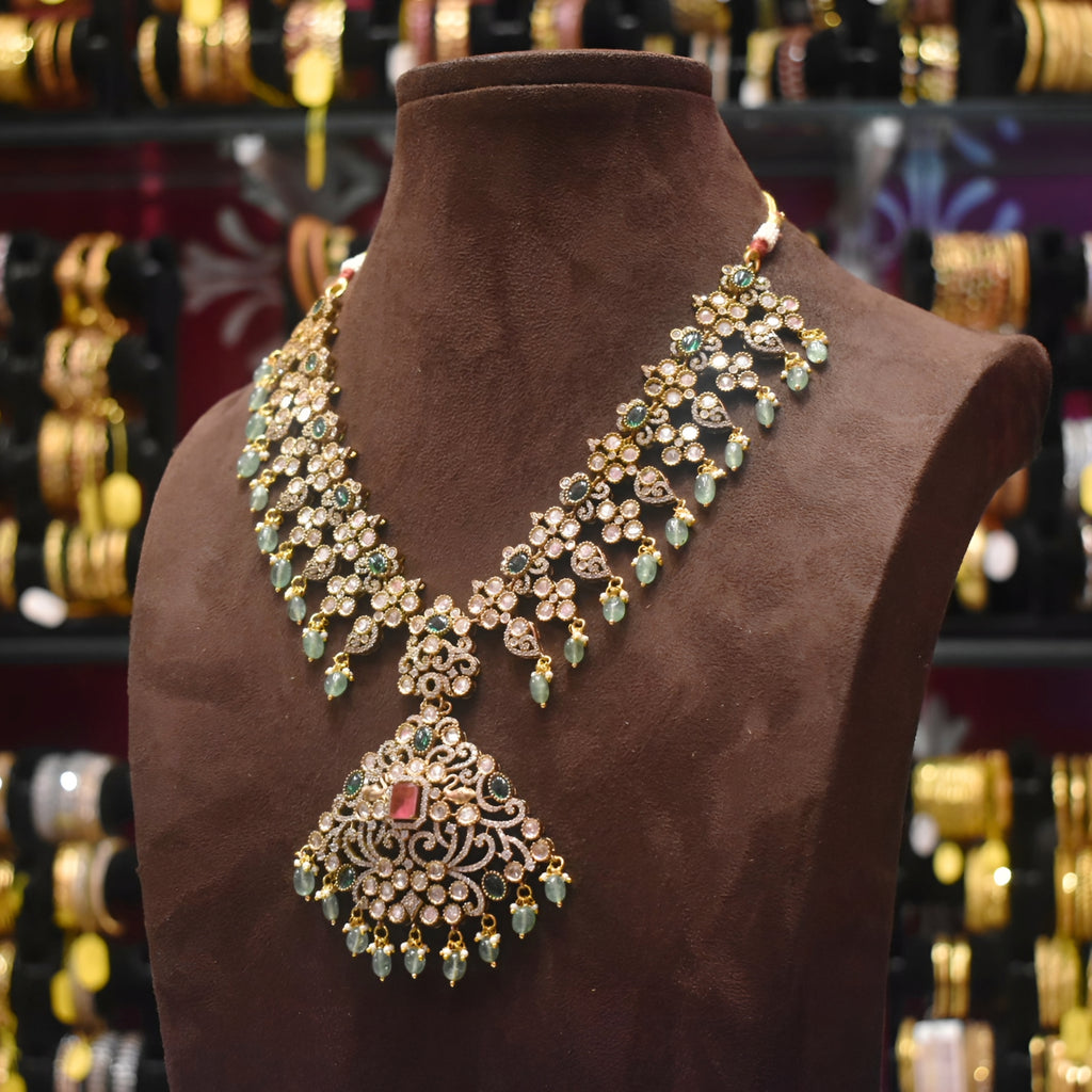 Ornate necklace with green and gold stones on a brown mannequin bust, with a blurred jewelry store background.