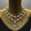 Ornate necklace with emerald green stones on a green velvet stand