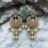 Ornate gold and green earrings on a marble surface with stone background