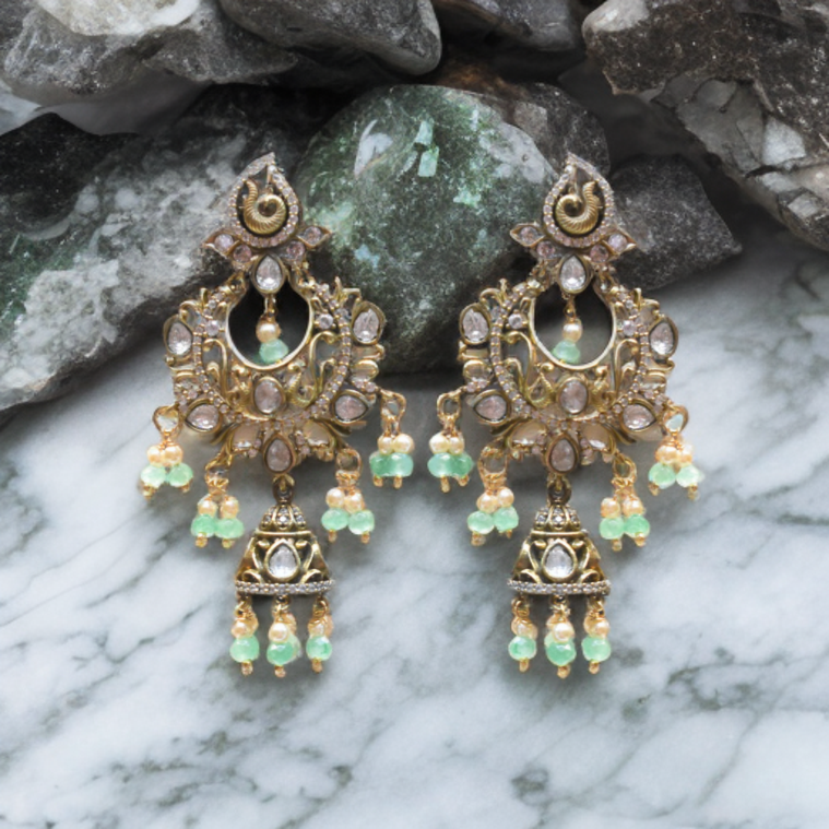 Ornate gold and green earrings on a marble surface with stone background