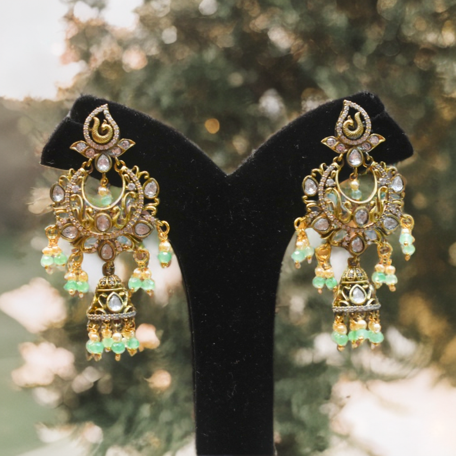 Ornate gold and green earrings on a black stand with a blurred natural background
