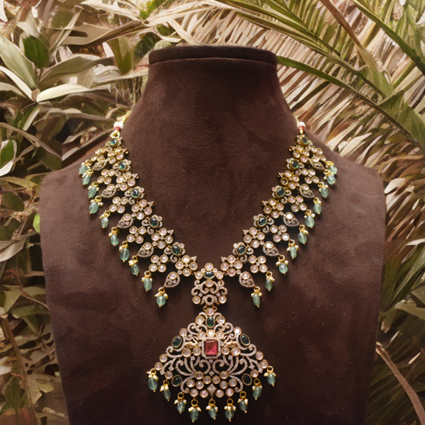 Ornate necklace with green and red stones on a brown mannequin against a leafy background