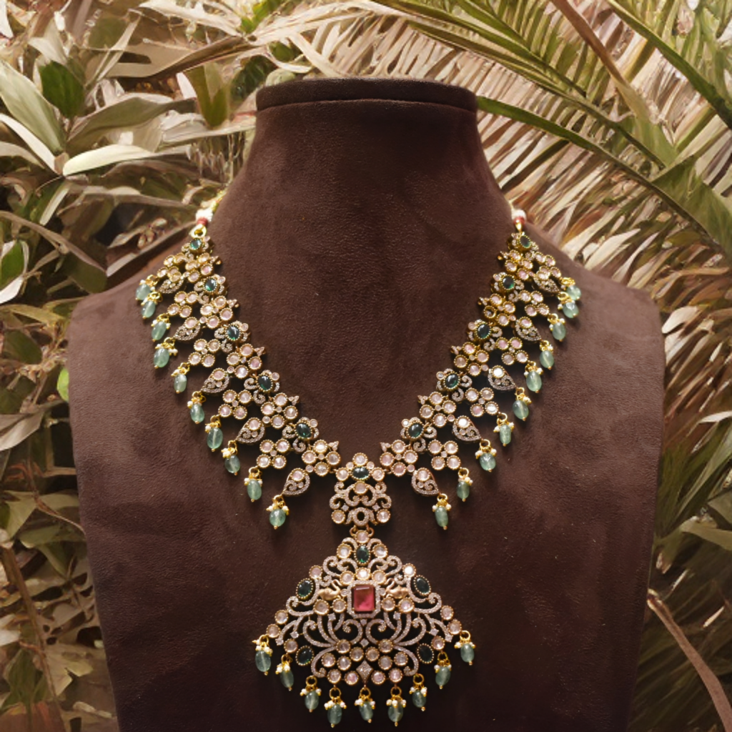 Ornate necklace with green and red stones on a brown mannequin against a leafy background
