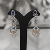 Pair of silver earrings with blue gemstones on a black stand against a blurred background