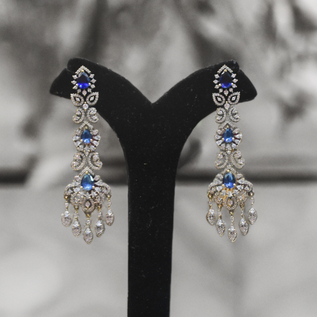 Pair of silver earrings with blue gemstones on a black stand against a blurred background
