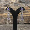 Pair of chandelier earrings with purple gemstones on a black stand against a stone background