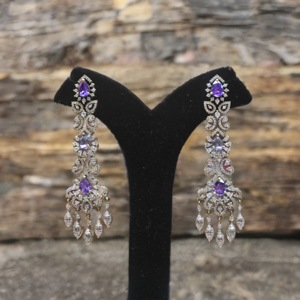 Pair of chandelier earrings with purple gemstones on a black stand against a stone background