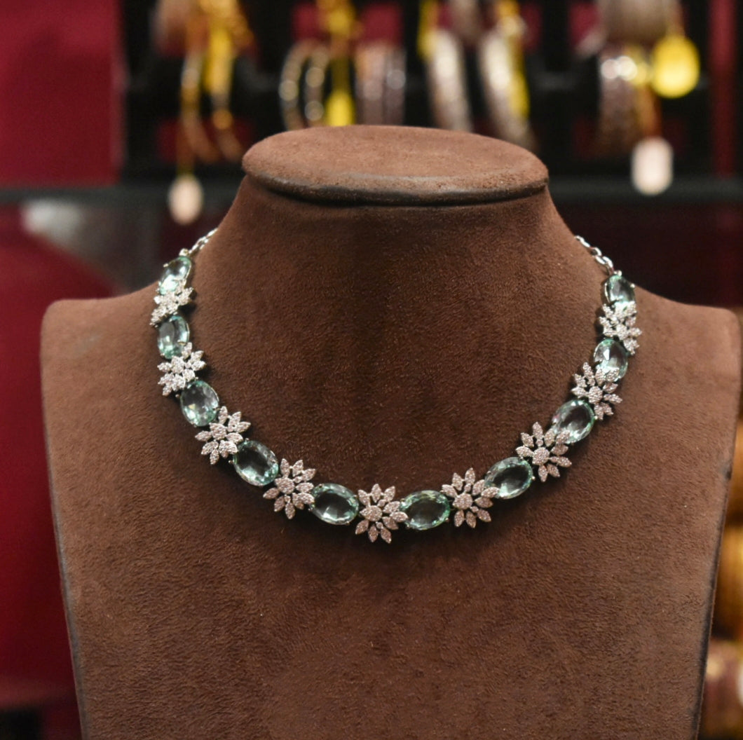 Necklace with green gemstones and floral designs on a brown velvet stand.