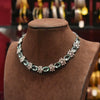 Necklace with green gemstones and silver flowers on a brown mannequin bust.