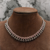 Necklace with red and clear stones on a brown velvet mannequin against a marble background