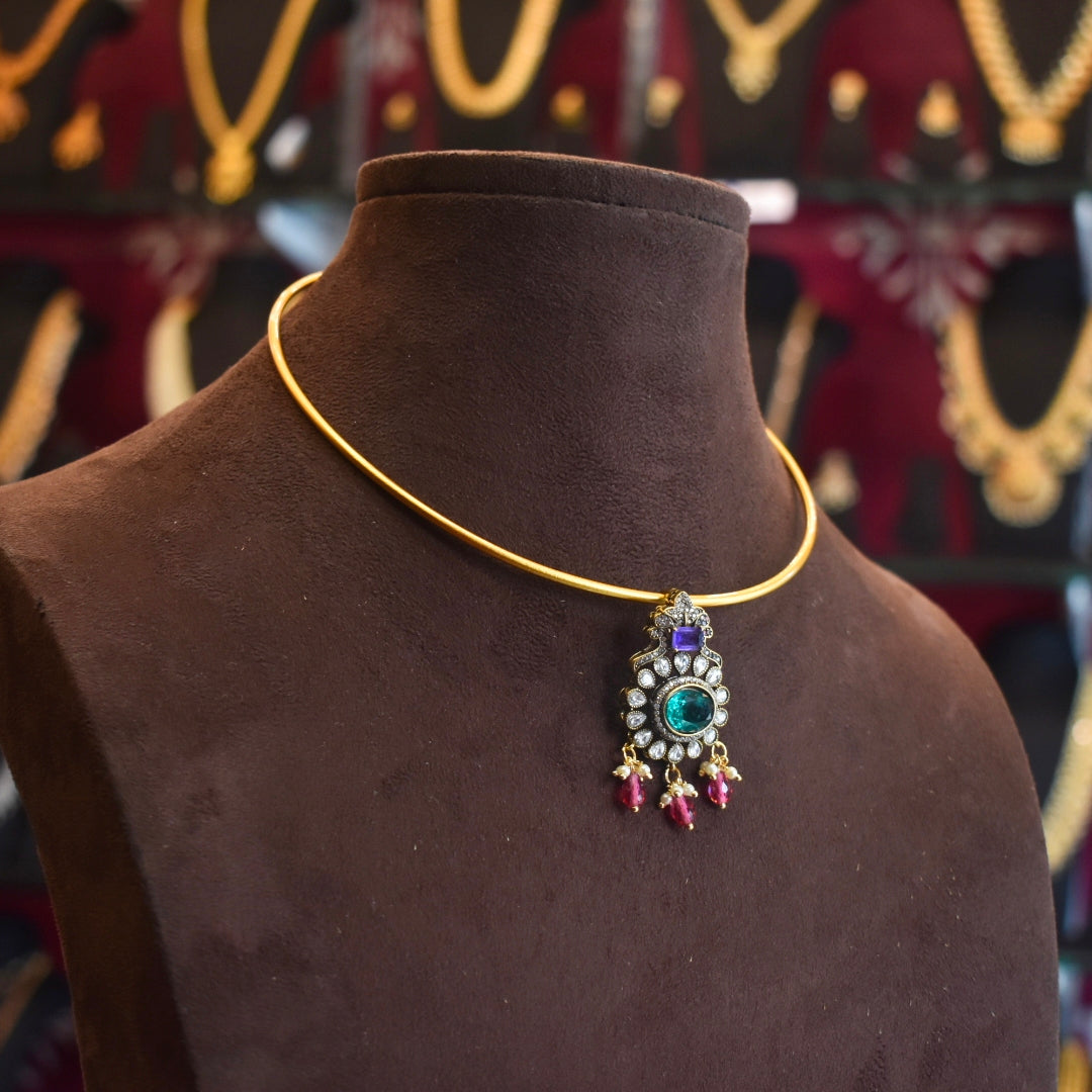 Gold necklace with a pendant on a brown mannequin against a blurred jewelry store background.