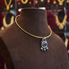 Gold necklace with a blue pendant on a brown mannequin against a blurred jewelry store background.