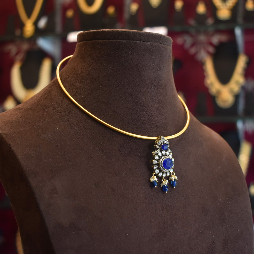Gold necklace with a blue pendant on a brown mannequin against a blurred jewelry store background.