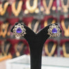 Pair of earrings with purple gemstones on a black stand against a blurred background