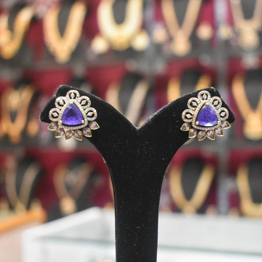 Pair of earrings with purple gemstones on a black stand against a blurred background