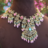 Ornate necklace with pink and green stones on a mannequin against a blurred floral background