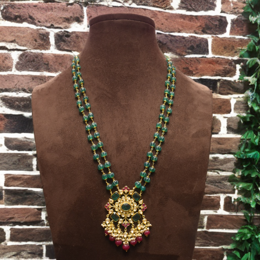 Decorative necklace with green and gold elements on a brown mannequin against a brick wall.