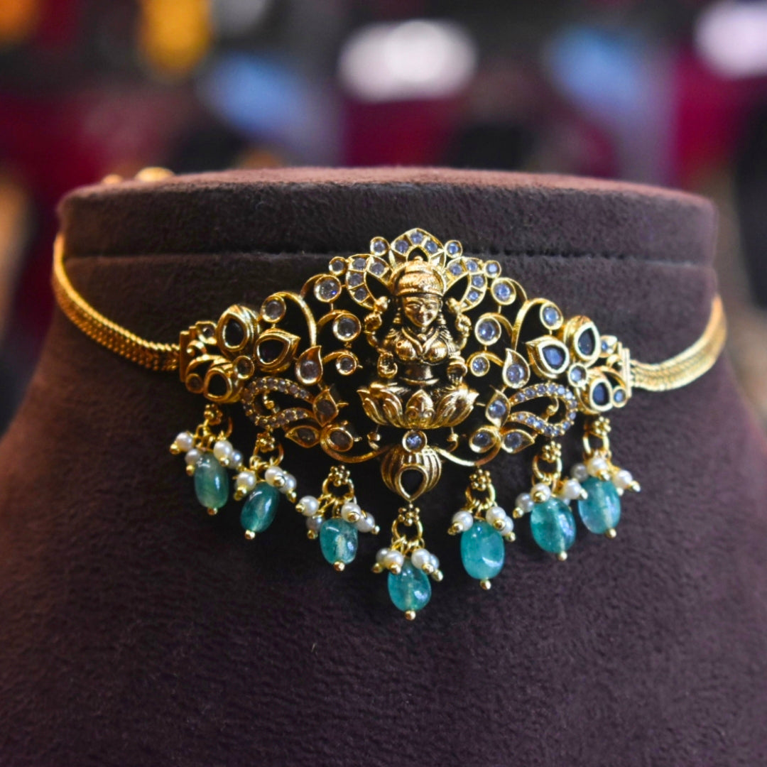 Gold and turquoise jewelry piece on a dark brown stand with a blurred background