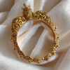 Gold bracelet with intricate design and lion heads on a white fabric background