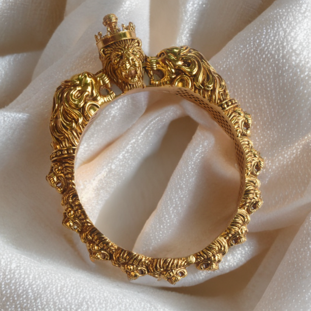 Gold bracelet with intricate design and lion heads on a white fabric background