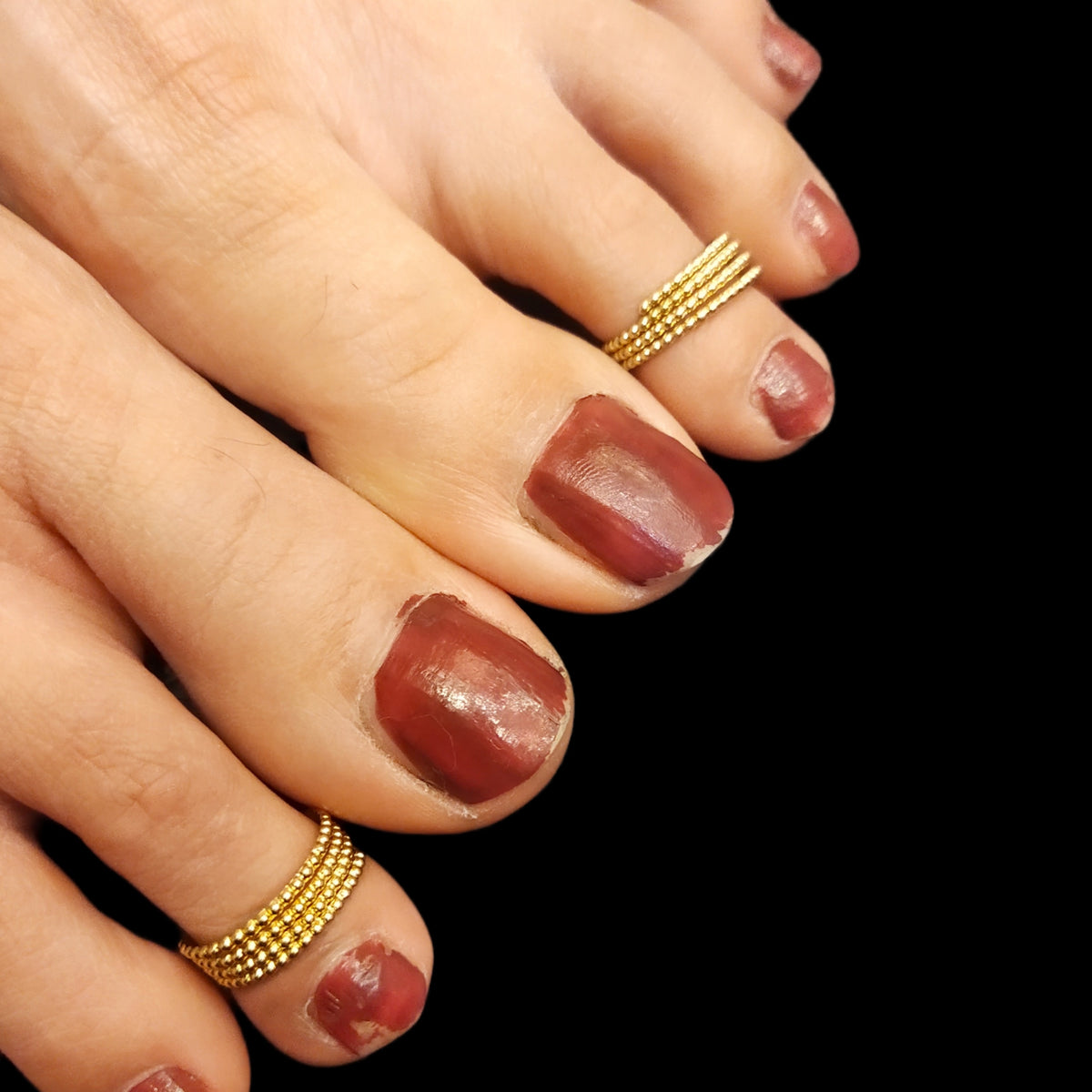 A close-up image of a woman's feet wearing gold-colored toe rings with a manicured toe nail and a small ring on the toe.