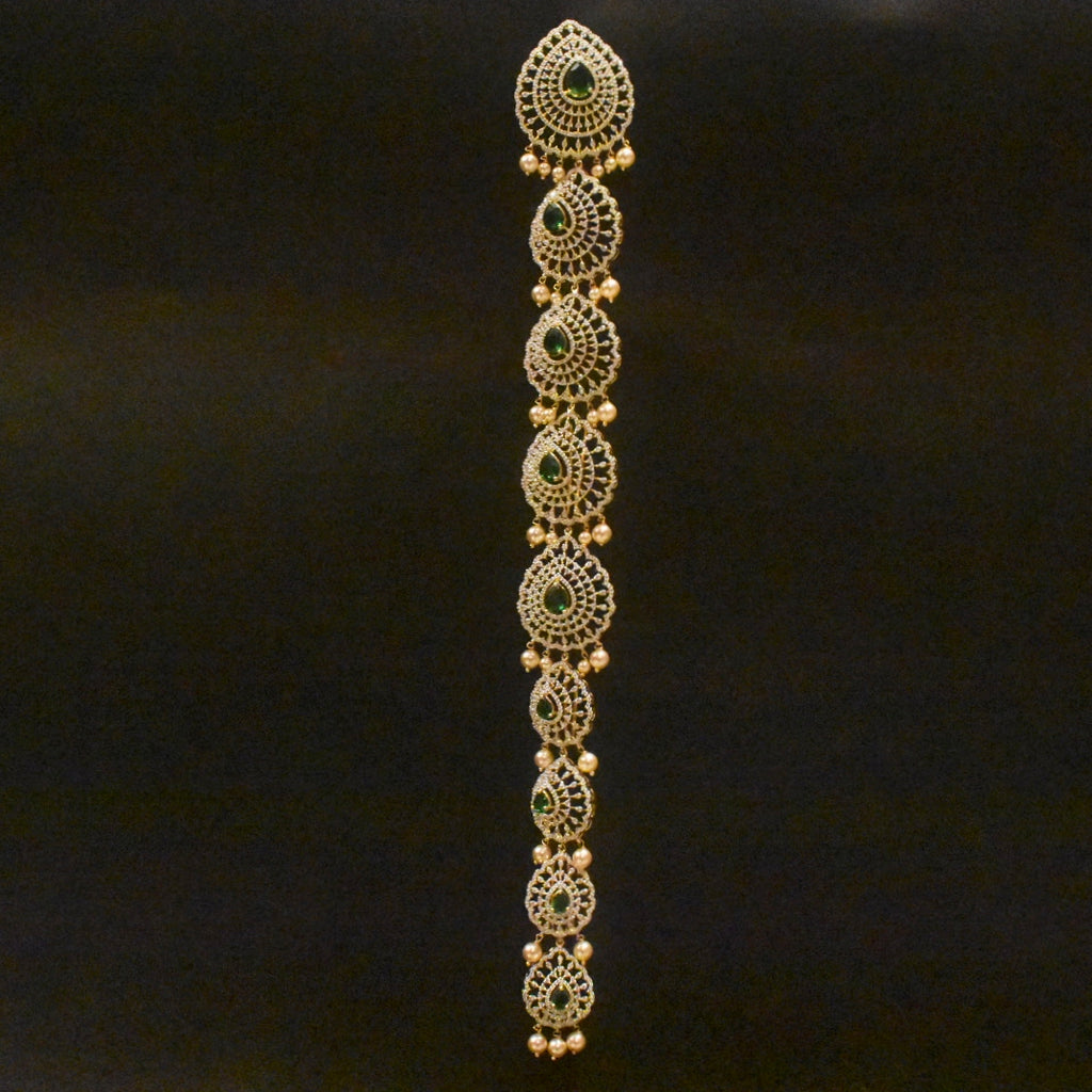 Decorative gold bracelet with green stones on a black background